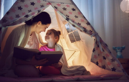 Mutter und Tochter lesen im Zelt im Kinderzimmer Eine Lese- oder Märchenstunde ist der perfekte Abschluss eines erfolgreichen Tages.