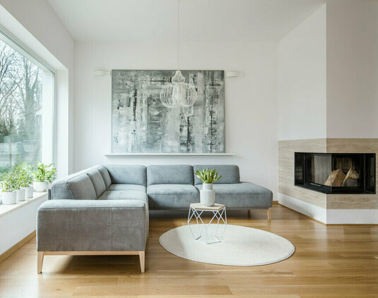Wohnzimmer mit Kamin Geräumiges weißes Wohnzimmer mit grauer Eckcouch, großem modernem Gemälde und Kamin.